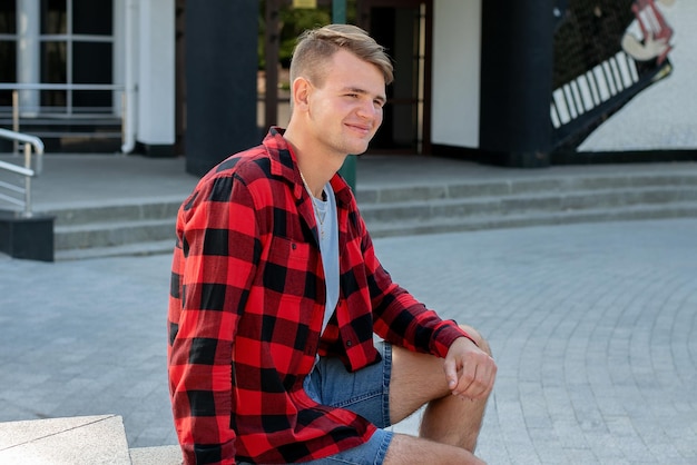 Happy, handsome Caucasian guy in a shirt in a cage sits on the street.