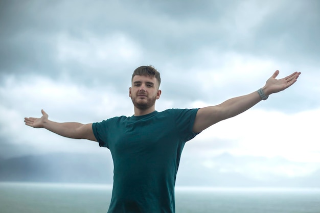 Happy handsome free guy young calm relaxed carefree man traveler with open raised hands enjoy sea ocean view person feeling good breath deep deeply fresh air Freedom travel happiness concept