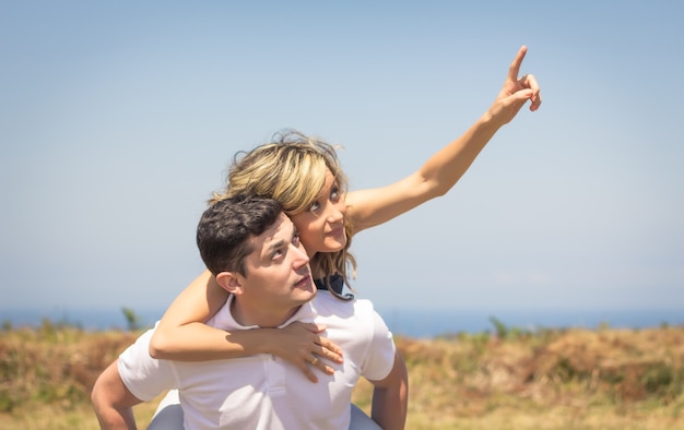 Happy handsome guy carrying his girlfriend on the back outdoors in a summer day over nature background