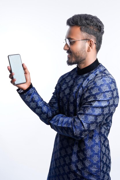 Happy handsome indian man wearing traditional outfit holding or using mobile phone celebrating diwali festival and giving expression