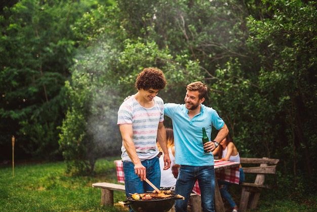 Happy handsome males preparing barbecue in the nature while the women are talking in the background