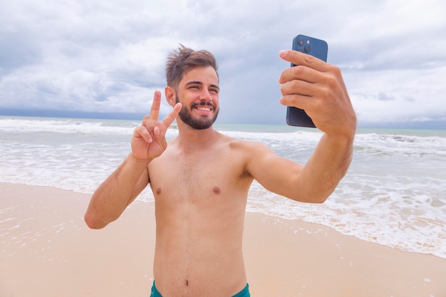 Happy handsome man making a selfie with smartphone at the beach Man on beach vacation taking photo with cellphone