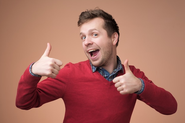 Happy handsome man in red sweater showing thumbs up