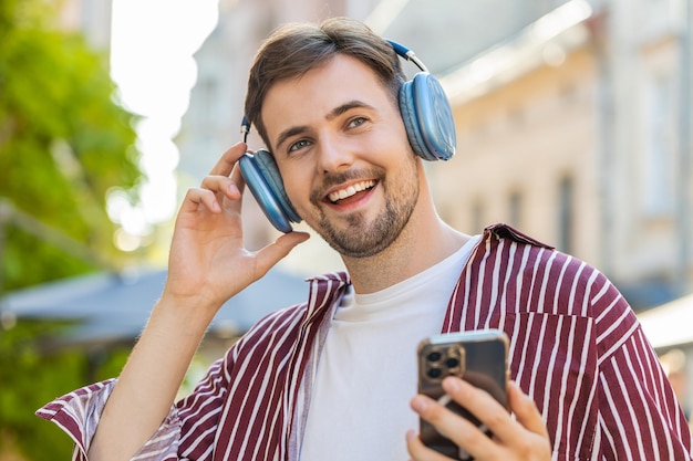 Happy handsome man in wireless headphones choosing listening music dancing outdoors city street