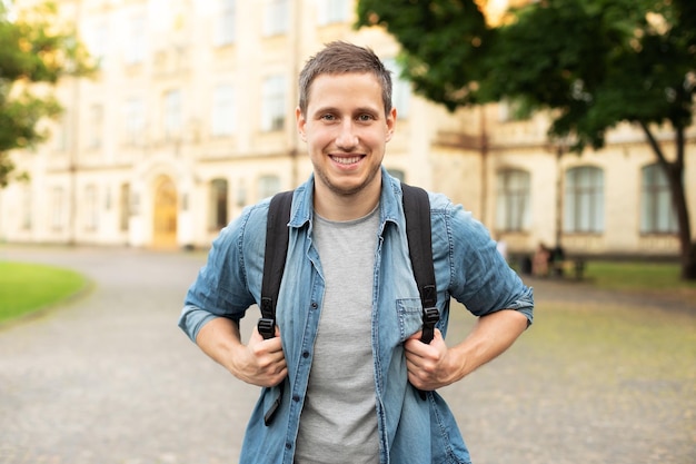 happy handsome man  with backpack on street walking in the park in summer