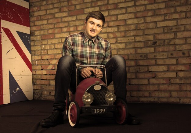 Happy Handsome Young Man Sitting on Vintage Toy Car While Looking at the Camera.