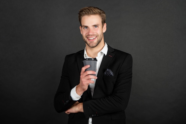 Happy handsome young man in suit with takeaway coffee