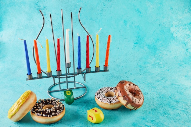 Happy hanukkah e hanukkah sameach - candeliere ebraico tradizionale con candele, ciambelle e trottole su sfondo blu. iscrizione in lettere dell'alfabeto ebraico nun, pei. gimel, ehi