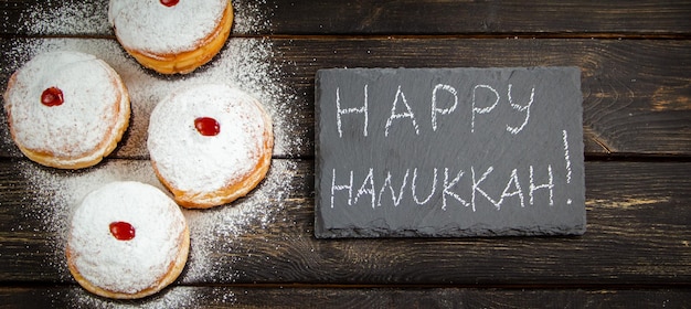 Happy Hanukkah Traditional dessert Sufganiyot on dark wooden background Donuts candles and gifts Celebrating Jewish holiday