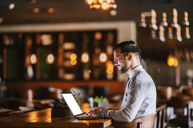 A happy hardworking young businessman is typing report on a laptop while working on a laptop