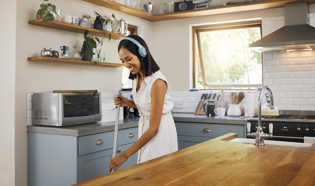 Happy headphones and woman cleaning the kitchen while listening to music podcast or radio Happiness smile and girl cleaner or housewife washing the floors in a modern home house or apartment