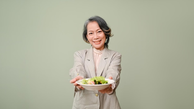 Счастливая и здоровая женщина 60-х годов, держащая тарелку с салатом, улыбается и смотрит в камеру