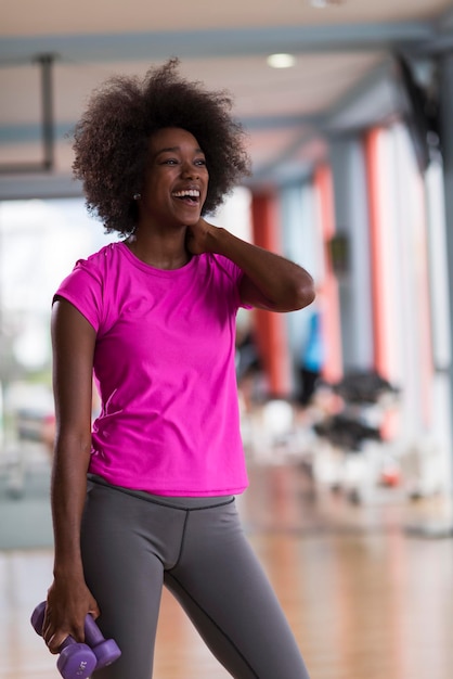 Happy healthy african american woman working out in a crossfit\
gym on weight loss with dumbbells