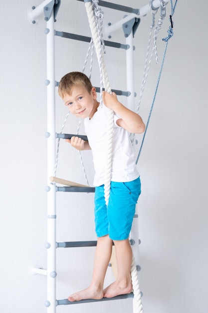 Happy healthy baby boy does sports on the swedish wall of the\
house healthy lifestyle sports at home children\'s sports complex\
ladder