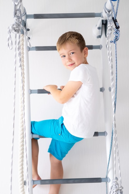 Happy healthy baby boy does sports on the Swedish wall of the house healthy lifestyle sports at home children's sports complex ladder