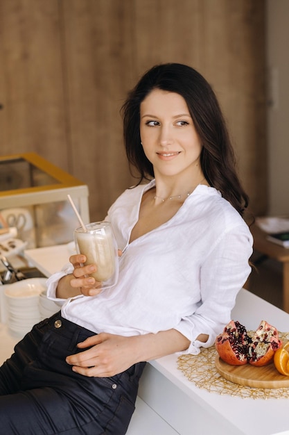 Una donna felice e sana tiene in mano un cocktail di frutta in piedi a casa in cucinamangiare sano