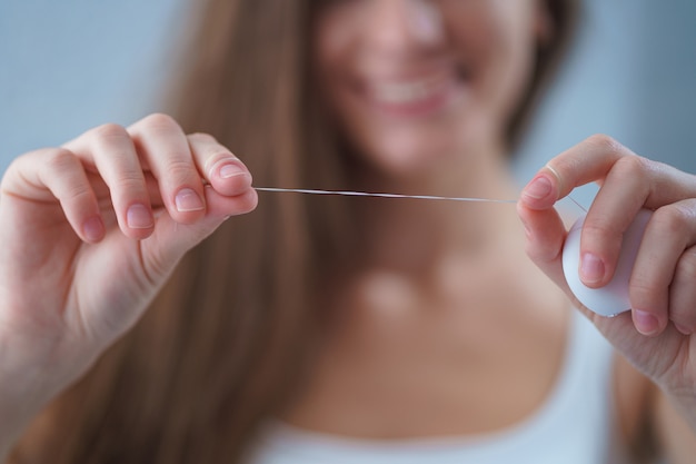 Photo happy healthy woman uses dental floss for brushing teeth and oral hygiene at home. teeth oral care