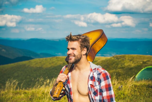 セクシーな男の自然の肖像画で美しい景色の週末を見てギターと幸せなハイカー男