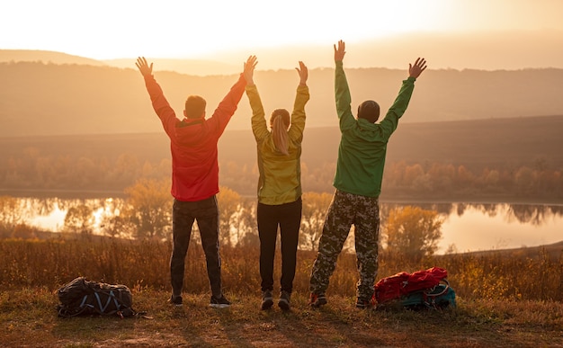 Happy hikers with arms raised enjoying sunset in nature