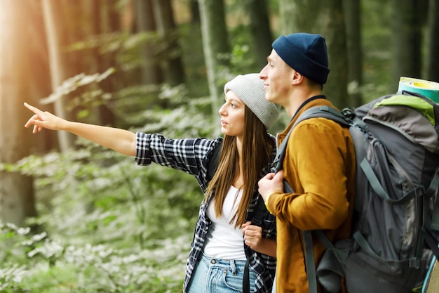 Happy hiking couple woman and man looking for direction the way to go in the forest and speaking to each other