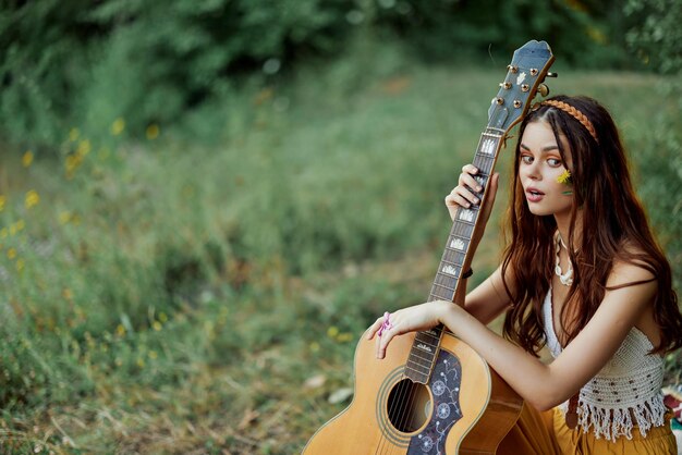 Happy hippie woman with a guitar relaxing in nature sitting on a plaid smiling and enjoying the view Lifestyle in harmony with nature and self High quality photo