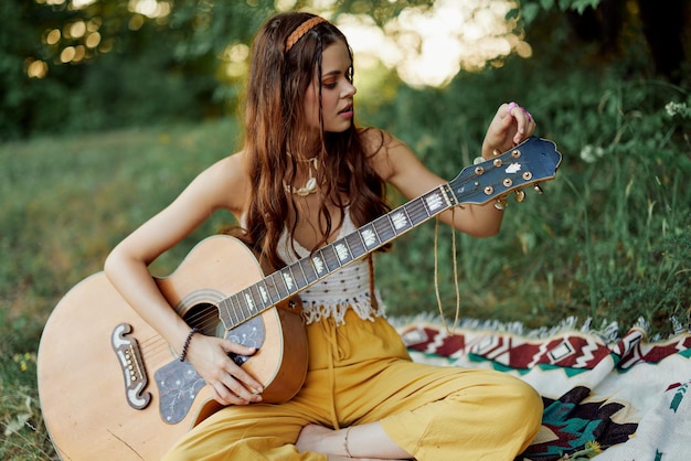Счастливая женщина-хиппи с гитарой улыбается, сидя на природе у озера