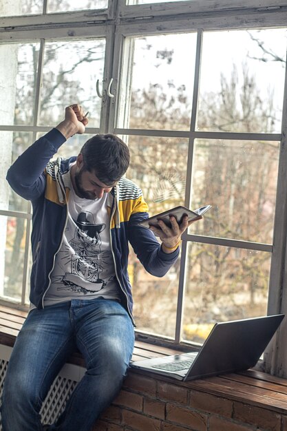 Happy hipster bearded man using laptop or notebook and notepad with pen