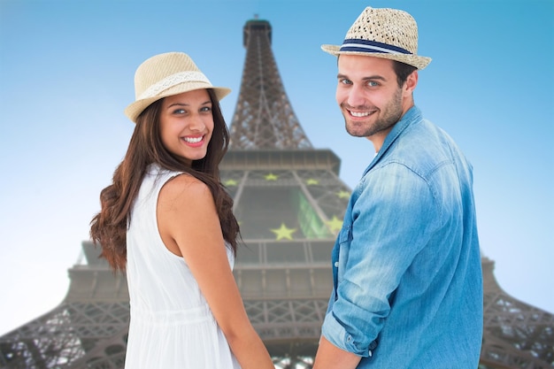 Coppie felici dei pantaloni a vita bassa che si tengono per mano e che sorridono alla macchina fotografica contro la torre eiffel