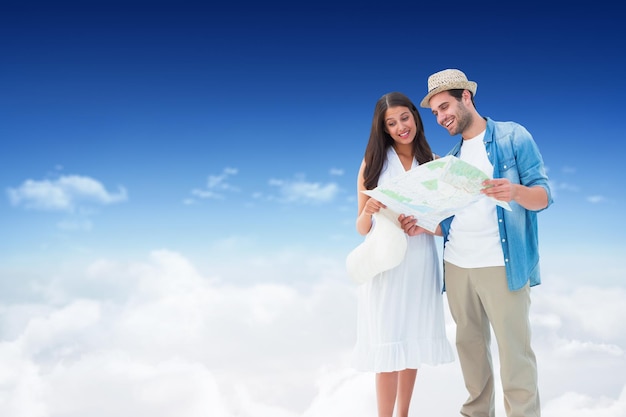 Happy hipster couple looking at map against bright blue sky over clouds