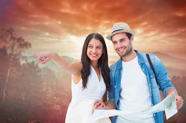 Happy hipster couple looking at map against sunrise over mountains