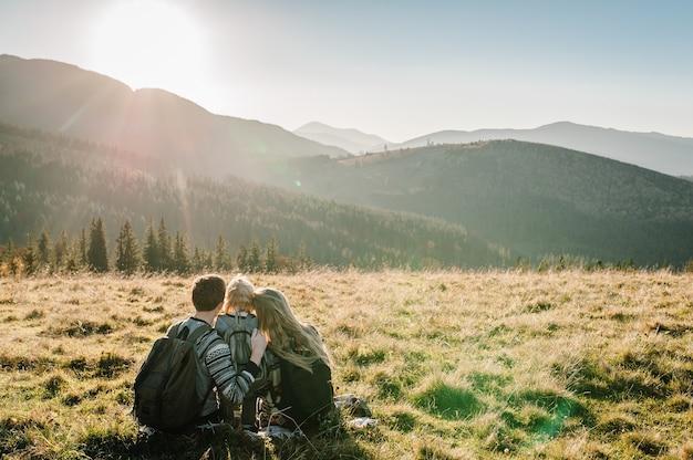 Happy hipster family mom, dad, daughter with backpack enjoying sunset on peak of foggy mountain