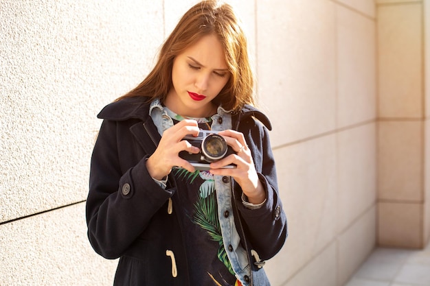 Happy hipster girl making photo with retro camera on city street. Travel concept. Sun flare