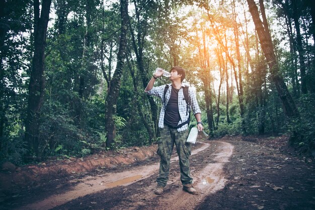 自然の森の中でハイキングしながら、リュックサックの男性の観光客がリュックサックの飲み水を楽しんでいます。