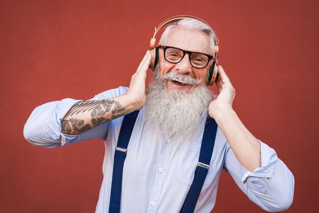 Foto uomo anziano felice dei pantaloni a vita bassa che ascolta la musica della playlist all'aperto nella città