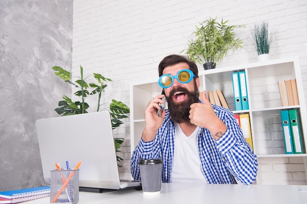 Happy hipster show approval hand gesture talking on mobile phone using computer for running business online thumbs up