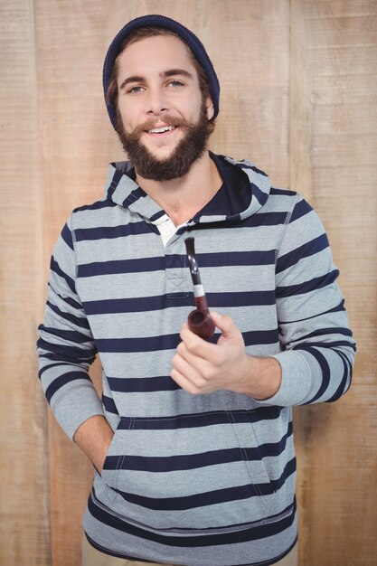 Happy hipster with hooded shirt holding smoking pipe