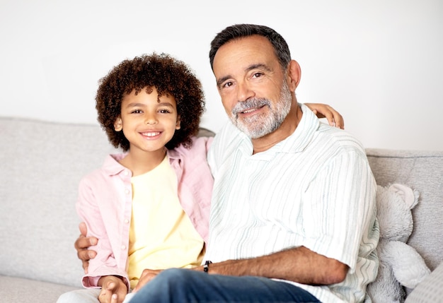 Happy hispanic little boy hugging his grandpa sitting at home