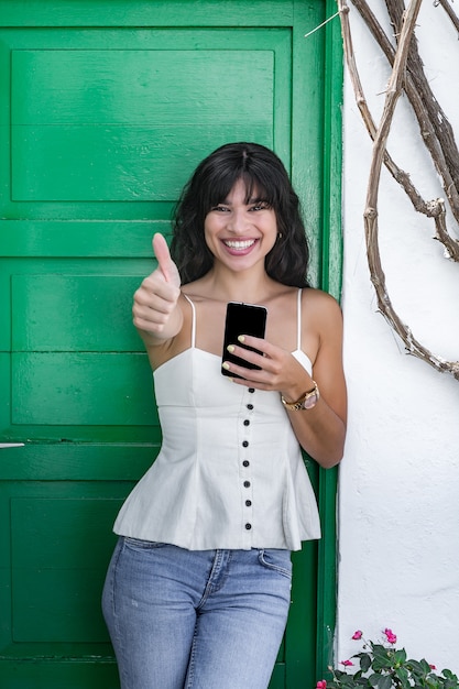 Happy Hispanic woman with smartphone gesturing thumb up