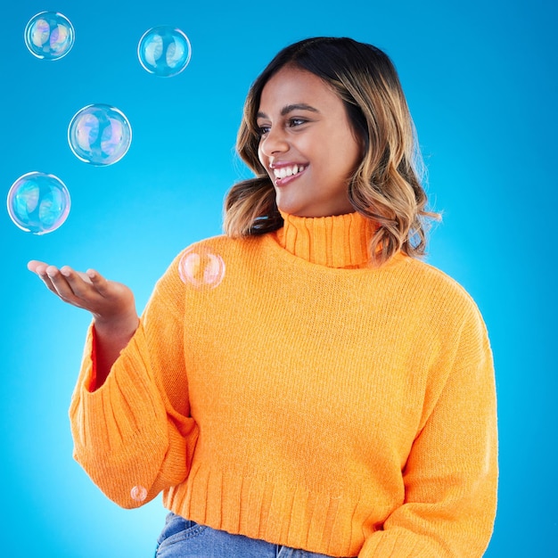 Happy holding and bubble with indian woman in studio for soap positive and satisfaction magic creative and smile with female isolated on blue background for bright cute and entertainment