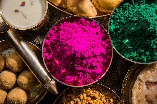 Поздравительная открытка Happy Holi, показывающая индийские традиционные сладкие и соленые блюда, цветы и порошковые цвета, расположенные на белом фоне или глине. Выборочный фокус