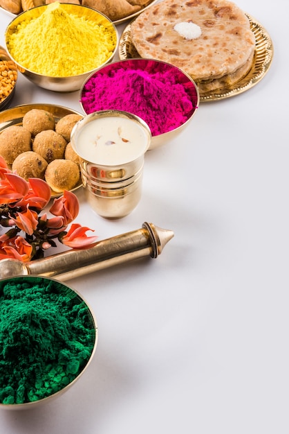 白い背景や粘土の上に配置されたインドの伝統的な甘くて塩辛い食べ物、花、粉の色を示すように設計されたハッピーホーリーグリーティングカード。セレクティブフォーカス