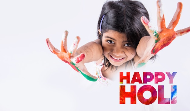 Фото Счастливое приветствие холи - милая маленькая индийская девочка с красочными руками, изолированные на белом фоне