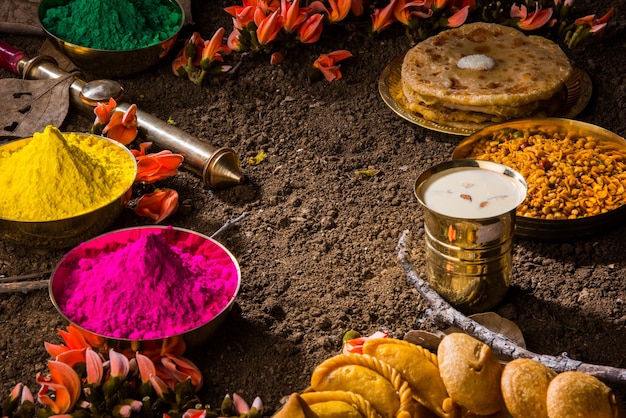 Happy holi-wenskaart ontworpen met indiase traditionele zoete en zoute gerechten, bloemen en poederkleuren gerangschikt op witte achtergrond of klei. selectieve focus