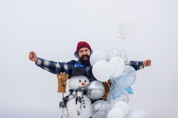 Happy holiday bearded man with snowman handmade snowman in hat scarf gloves with air balloons