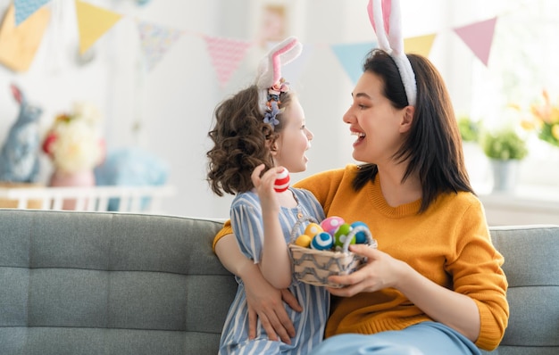 Happy holiday! Mother and her daughter with painting eggs. Family celebrating Easter. Cute little child girl is wearing bunny ears.