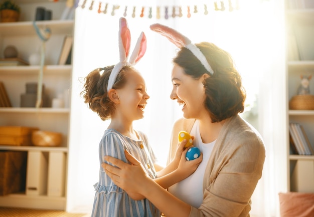 Happy holiday Mother and her daughter with painting eggs Family celebrating Easter Cute little child girl is wearing bunny ears