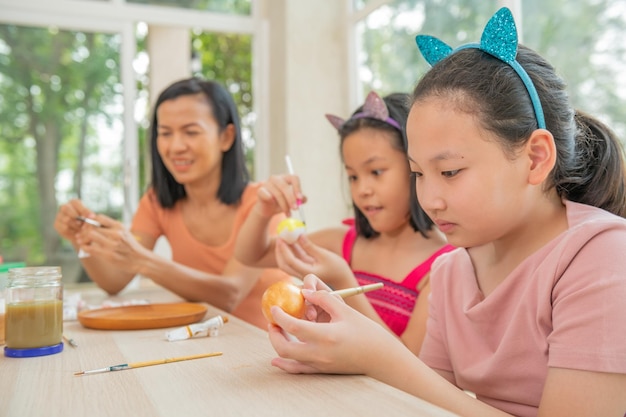 Happy holiday Mother and her two daughter painting eggs Happy family preparing for Easter Asian cute little child girl wearing bunny ears