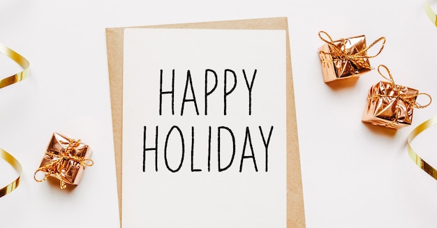 Happy holiday note with envelope, gifts and gold ribbon on white background