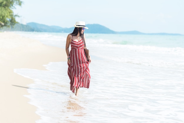 Foto buone vacanze ed estate. l'estate d'uso sorridente di modo della donna asiatica che cammina sull'oceano sabbioso beac