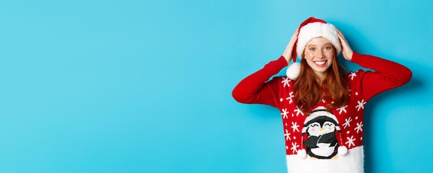 Foto buone vacanze e concetto di natale bella ragazza rossa in maglione di natale indossa cappello di babbo natale e smilin